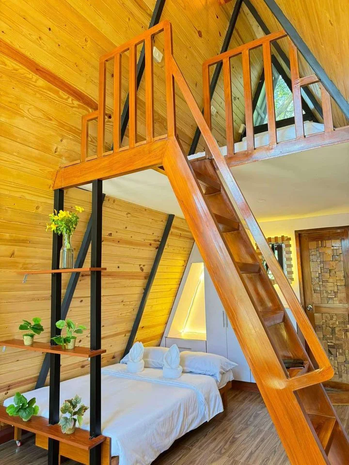 Warm timber cabin interior with a loft, staircase, and queen bed