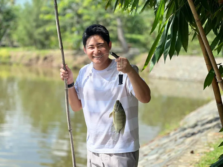A guest holding a caught fish beside the farmhouse pond